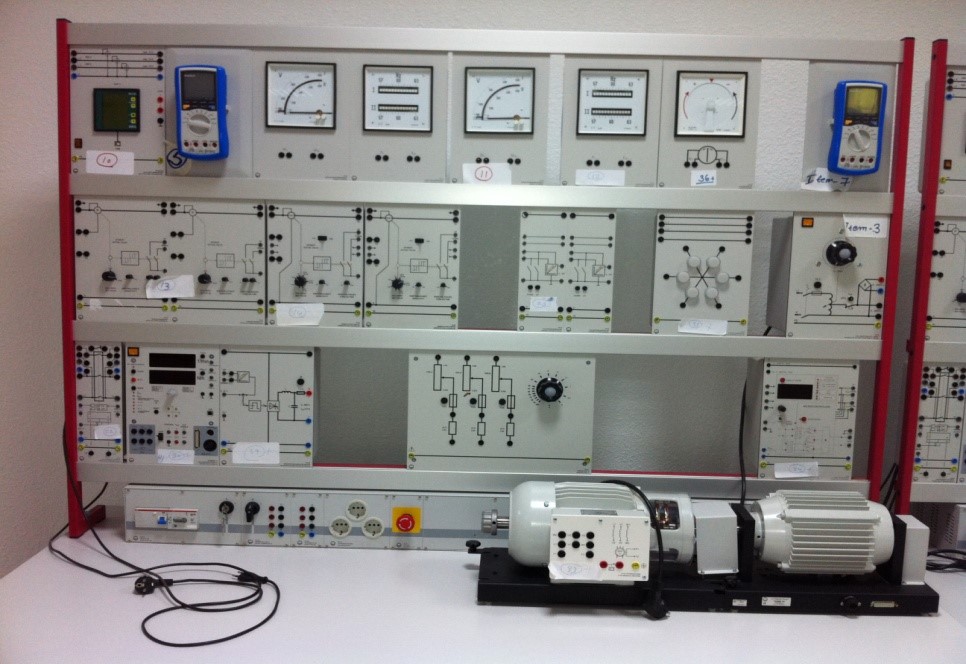 A control panel with various gauges, meters, and circuit diagrams, alongside a motor setup on a workbench.