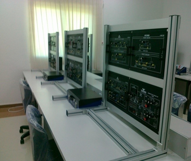 A classroom with multiple workstations featuring electronic equipment and control panels, illuminated by natural light.