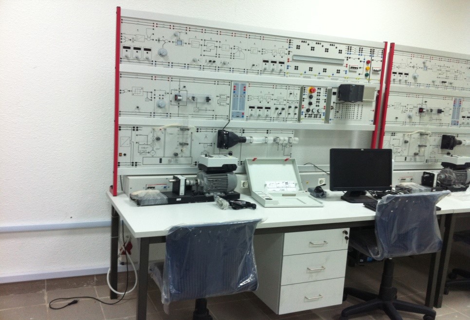 A technical workspace featuring a control panel with various components, a computer, and equipment on a desk.