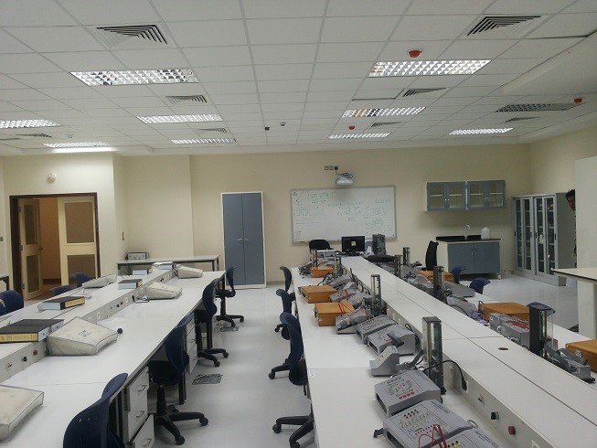 A spacious laboratory with multiple workstations, computers, and equipment, featuring a whiteboard and storage cabinets.