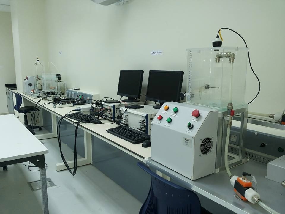 A laboratory setup featuring computers, equipment, and a transparent apparatus with control buttons on a workbench.